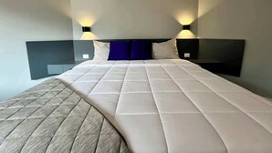 Una camera d'albergo con un letto grande, due comodini e illuminazione a parete.