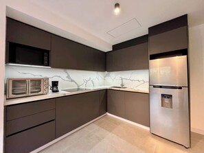 A modern kitchen with dark cabinetry, a marble backsplash, a built-in microwave, and a stainless steel refrigerator. - Moderno Ph en Altamira con hermosa vista al Ávila (Caracas)