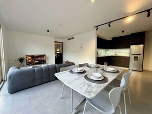 A modern living room with a sectional sofa, a dining table set with plates and glasses, and a kitchen area with a refrigerator. - Moderno Ph en Altamira con hermosa vista al Ávila (Caracas)
