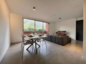 Una sala de estar moderna con comedor, ventanas grandes y televisor de pantalla plana.