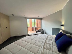 Un dormitorio moderno con una cama grande, una silla y un ventanal corredera que da a un espacio exterior.