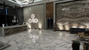 Un hall d’entrée moderne avec un sol en marbre, un comptoir d’accueil et deux grands luminaires circulaires.