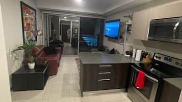 Una cocina moderna con una isla central, microondas integrado y horno. Hay una zona de comedor con un sofá y televisor.