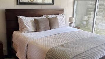 A bedroom with a bed, pillows, a nightstand, a framed artwork, and a window.