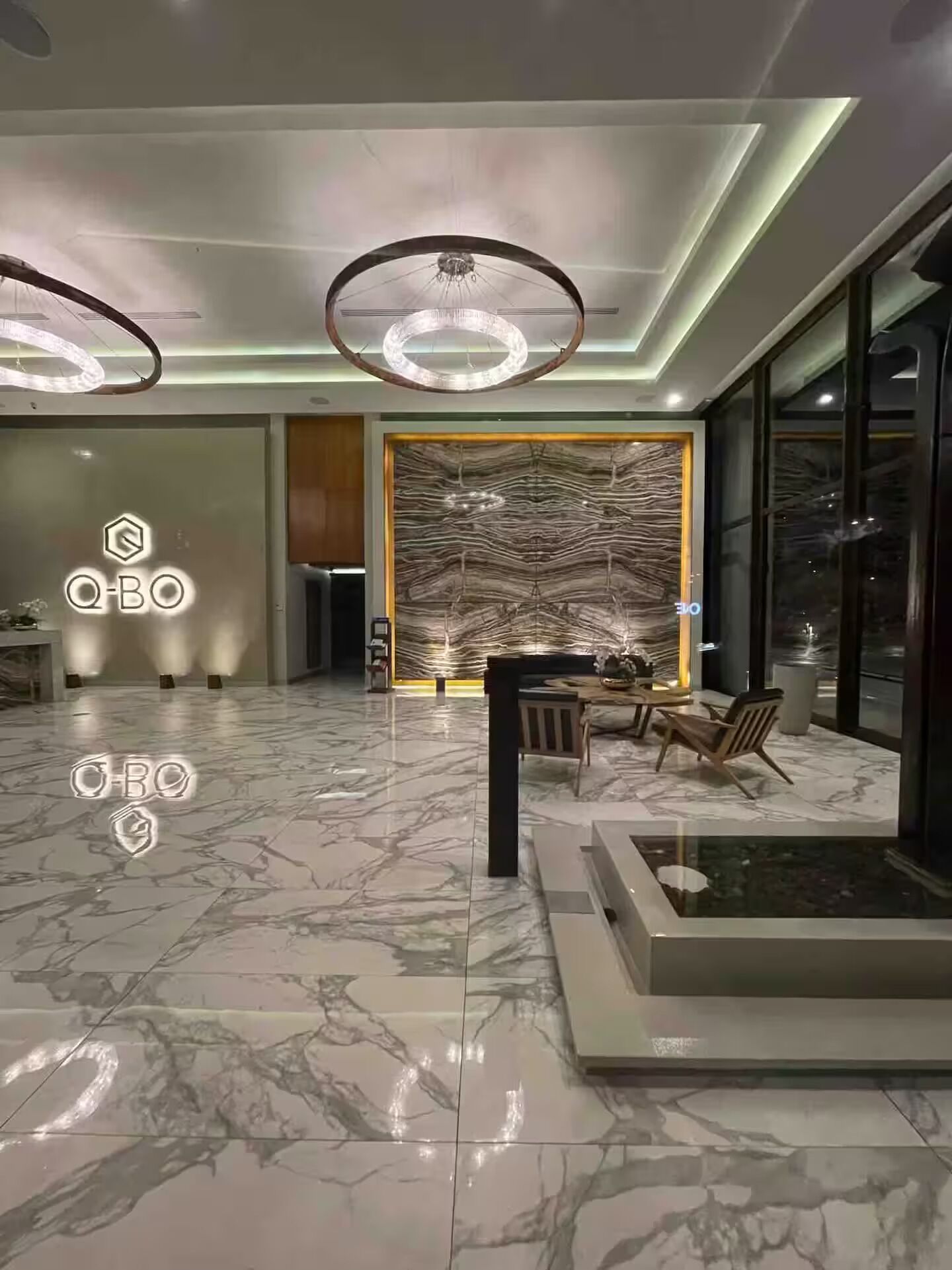 A modern interior with a marble floor, a dining area with chairs and a table, and a large wall with a textured pattern.