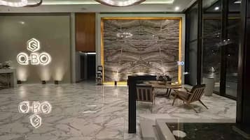 A modern interior with a marble floor, a dining area with chairs and a table, and a large wall with a textured pattern.