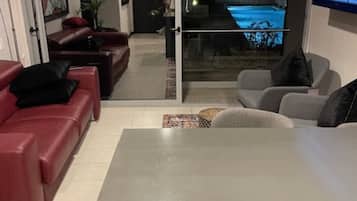 Una sala de estar moderna con un televisor grande, comedor y vista a una piscina por la noche.