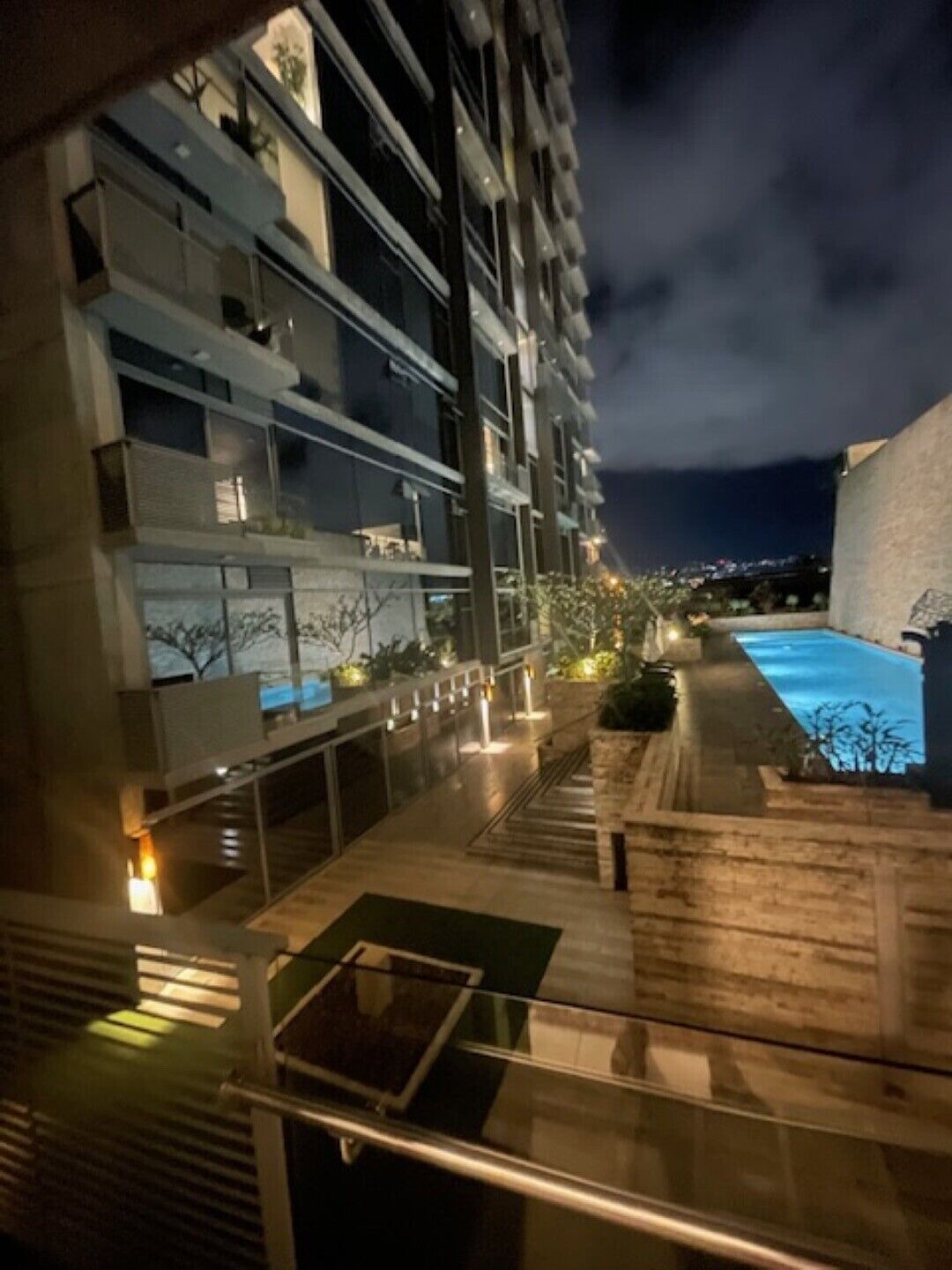 A nighttime view of a modern building with multiple balconies, a swimming pool, and outdoor lighting.