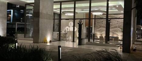 A modern building entrance with glass doors, a concrete pillar, and a well-lit interior.