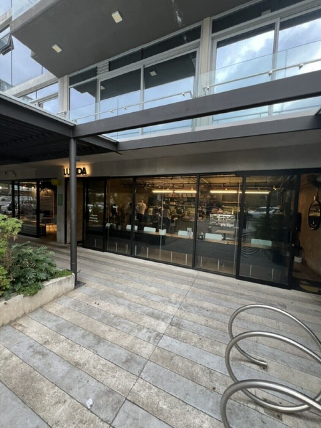 Un bâtiment moderne doté d’une façade vitrée et d’un espace extérieur couvert avec un banc en métal.