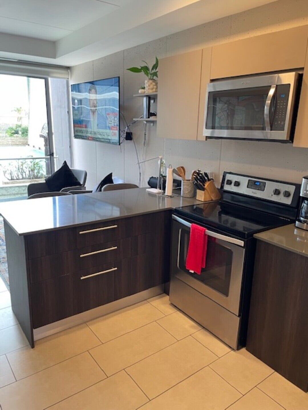 A modern kitchen with dark cabinetry, a stainless steel oven, a microwave, and a dining area with a table and chairs.