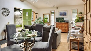Uma sala de estar acolhedora com uma mesa de vidro, poltronas estofadas cinzas, uma porta verde e uma televisão.