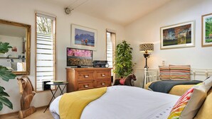 Quarto com cama, penteadeira, televisão e uma planta.