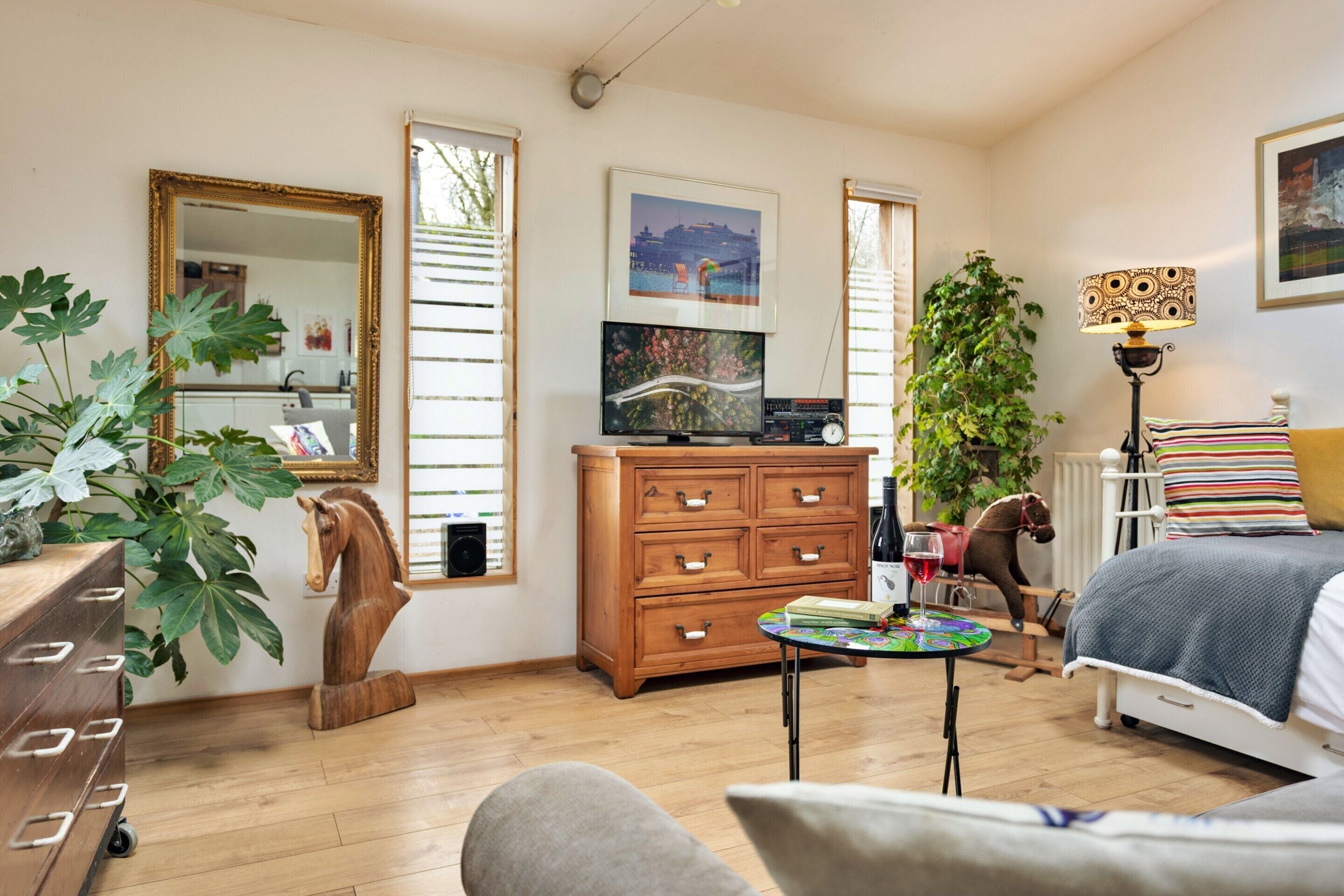 Een slaapkamer met een bed, dressoir, televisie en een groot raam.