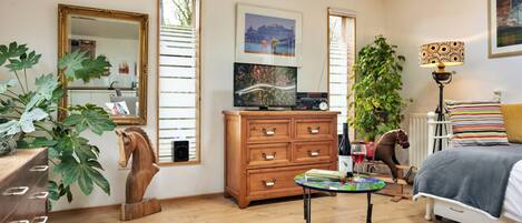 Een slaapkamer met een bed, dressoir, televisie en een groot raam.