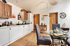 A modern kitchen with white cabinetry, wooden accents, and a dining area with a glass table and chairs. - Georgian Devon House With Hot Tub (Leyburn)