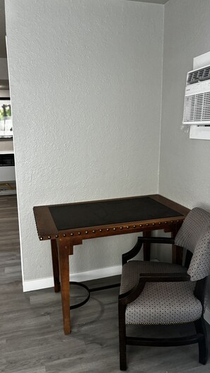 Ein Eckzimmer mit Holztisch und Stuhl, einer Wand mit Strukturmuster und einer sichtbaren Klimaanlage.