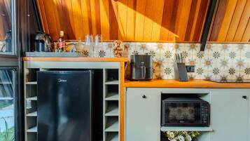 Cocina compacta equipada con refrigerador, microondas, cafetera y un lavamanos pequeño.