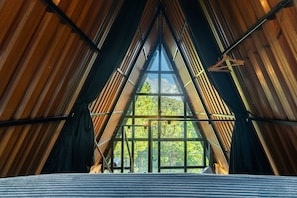 Una habitación con techo inclinado y ventanas amplias que ofrecen vistas a un paisaje boscoso.