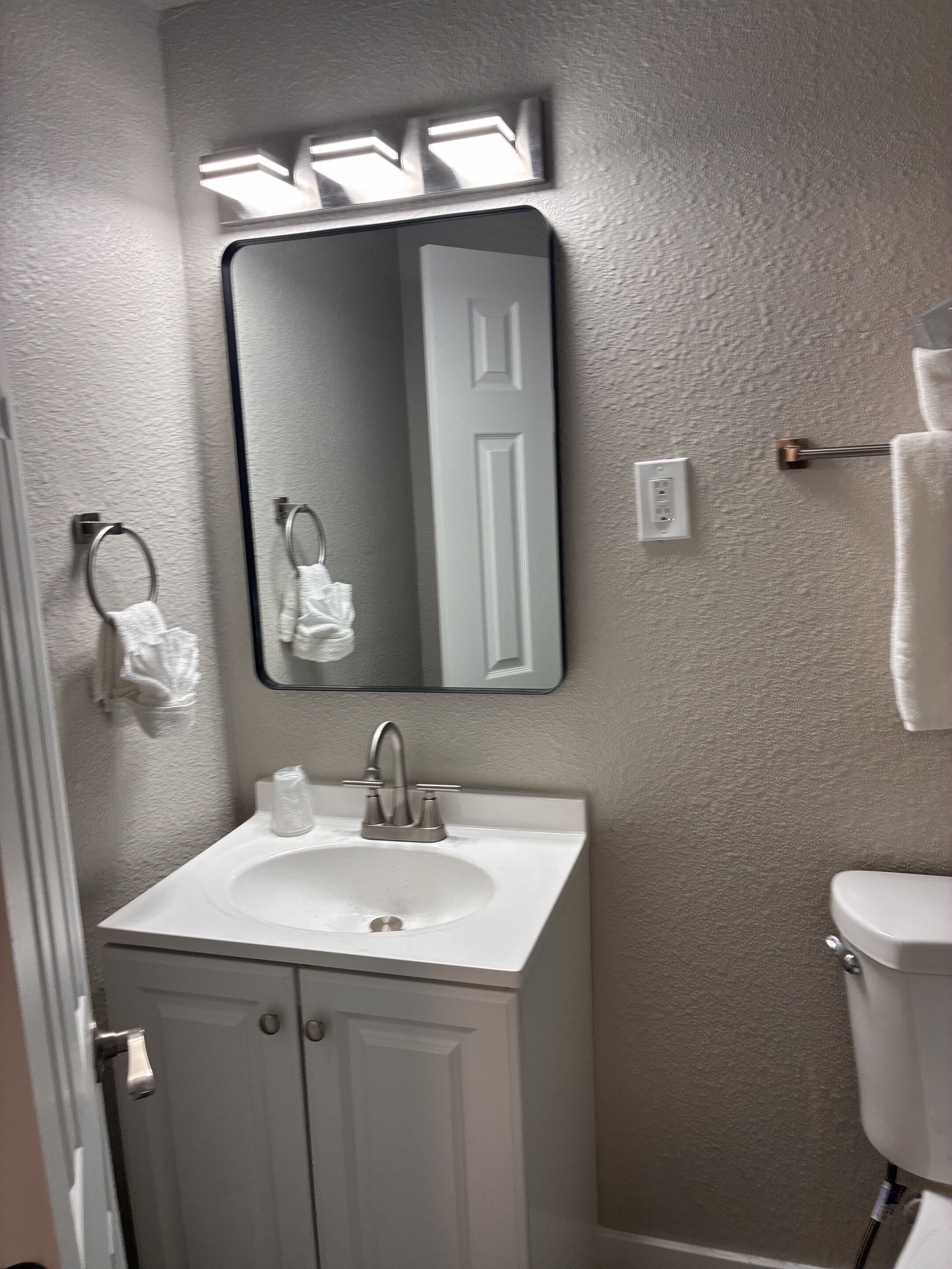 A bathroom with a white sink, a mirror, a towel rack, and a toilet.
