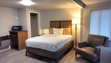 Quarto de hotel com uma cama, uma cadeira, uma mesa com micro-ondas e uma luminária.