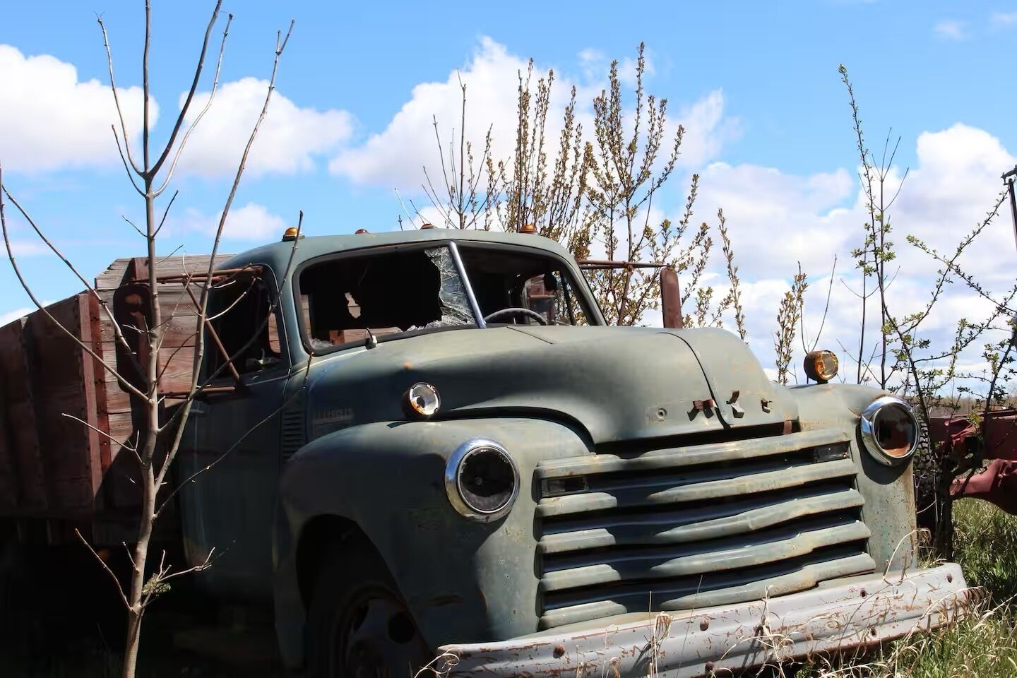 An old, rusted truck parked outdoors with a clear sky and bare trees in the background.