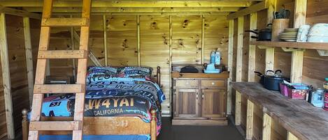 Interior de una cabaña de madera con un entrepiso con dormitorio, una zona de cocina y una cama para mascotas.