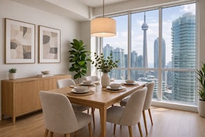Un coin repas avec une table dressée pour quatre personnes, une plante, un vase et des œuvres d’art encadrées accrochées au mur.