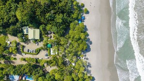 An aerial view of a beach resort with a pool, parking area, and dense tropical vegetation. - Deluxe family Bedroom - Beachfront - Manuel Antonio with AC (Manuel Antonio)