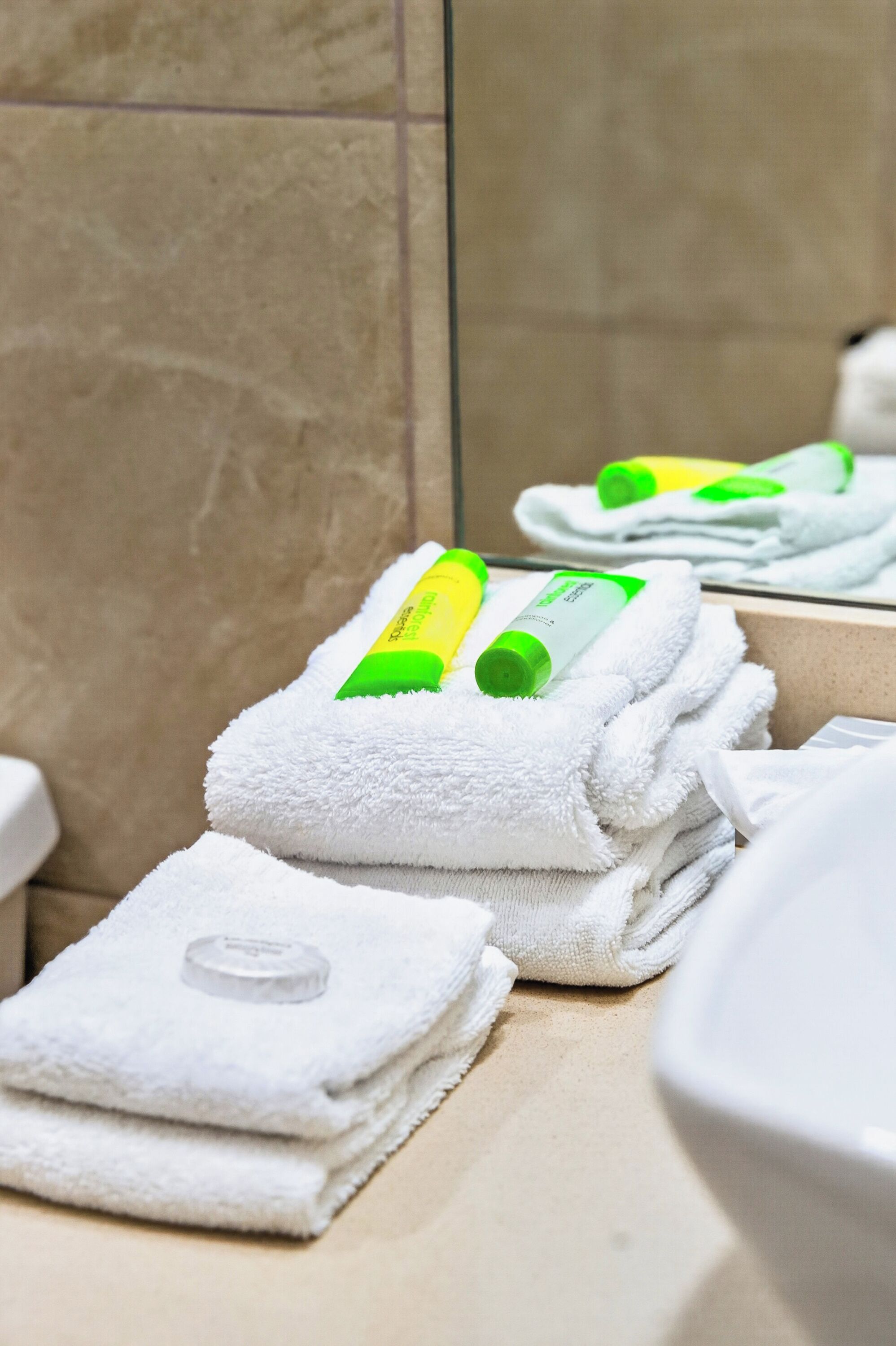 Une salle de bain avec des piles de serviettes blanches et des bouteilles vertes et jaunes posées dessus.