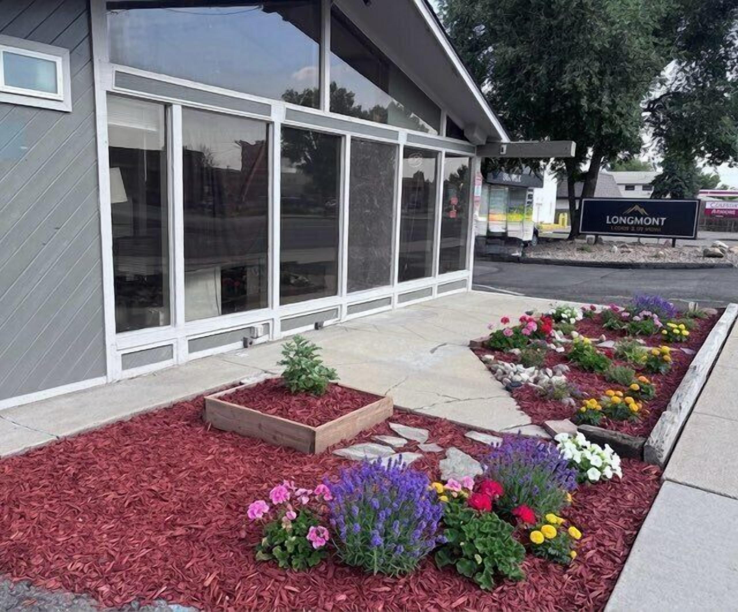 Un bâtiment doté de grandes fenêtres, une enseigne indiquant « LONGMONT », et un espace paysager agrémenté de parterres de fleurs.