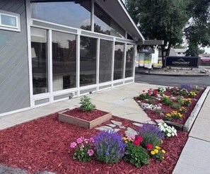 Un edificio con ventanas amplias, un cartel que dice 'LONGMONT' y un área ajardinada con macizos de flores.