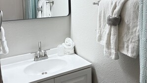 A bathroom with a white sink, a mirror, a towel rack with a towel, and a shower curtain.