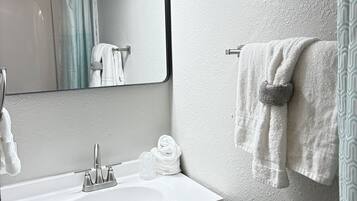Une salle de bain avec un lavabo blanc, un miroir, un porte-serviettes avec une serviette et un rideau de douche.