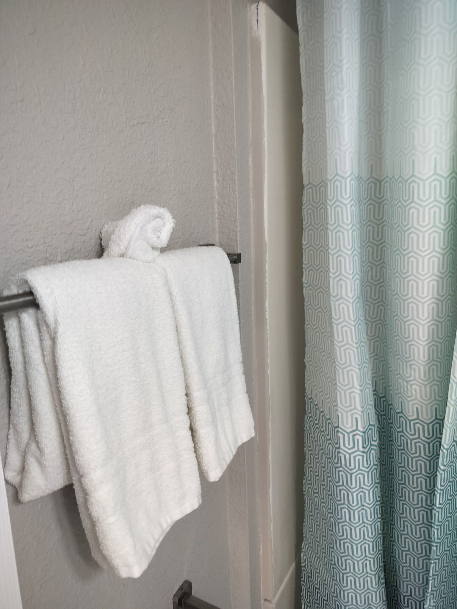 Ein Badezimmer mit Handtuchhalter, gefaltetem Handtuch, einem gemusterten Duschvorhang und einer schlichten Wand.