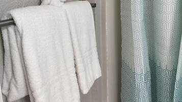Ein Badezimmer mit Handtuchhalter, gefaltetem Handtuch, einem gemusterten Duschvorhang und einer schlichten Wand.