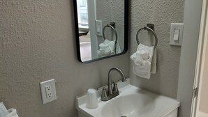 A bathroom with a white sink, a mirror, a towel ring, and a toilet. - Large Renovated Double Queen Studio (Longmont)