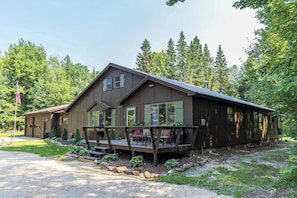 A two-story cabin with a porch, surrounded by trees. - Fall by Whitefish Bay | Sauna, Arcade, Sleeps 10 (Brimley)
