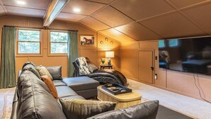 A cozy living room with a sectional sofa, a leather armchair, a coffee table, and a flat-screen TV mounted on the wall.