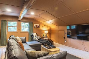 A cozy living room with a sectional sofa, a leather armchair, a coffee table, and a flat-screen TV mounted on the wall. - Fall by Whitefish Bay | Sauna, Arcade, Sleeps 10 (Brimley)