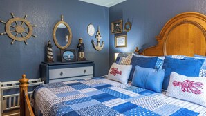 A bedroom with a bed, dresser, and nautical-themed decor.