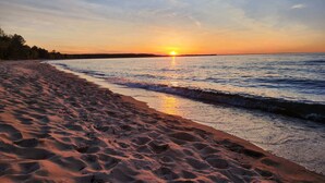 A beach with sand and water, a sunset in the background, and a clear sky.
