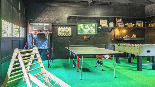 A recreational room with a basketball hoop, ping pong table, foosball table, and a climbing ladder.