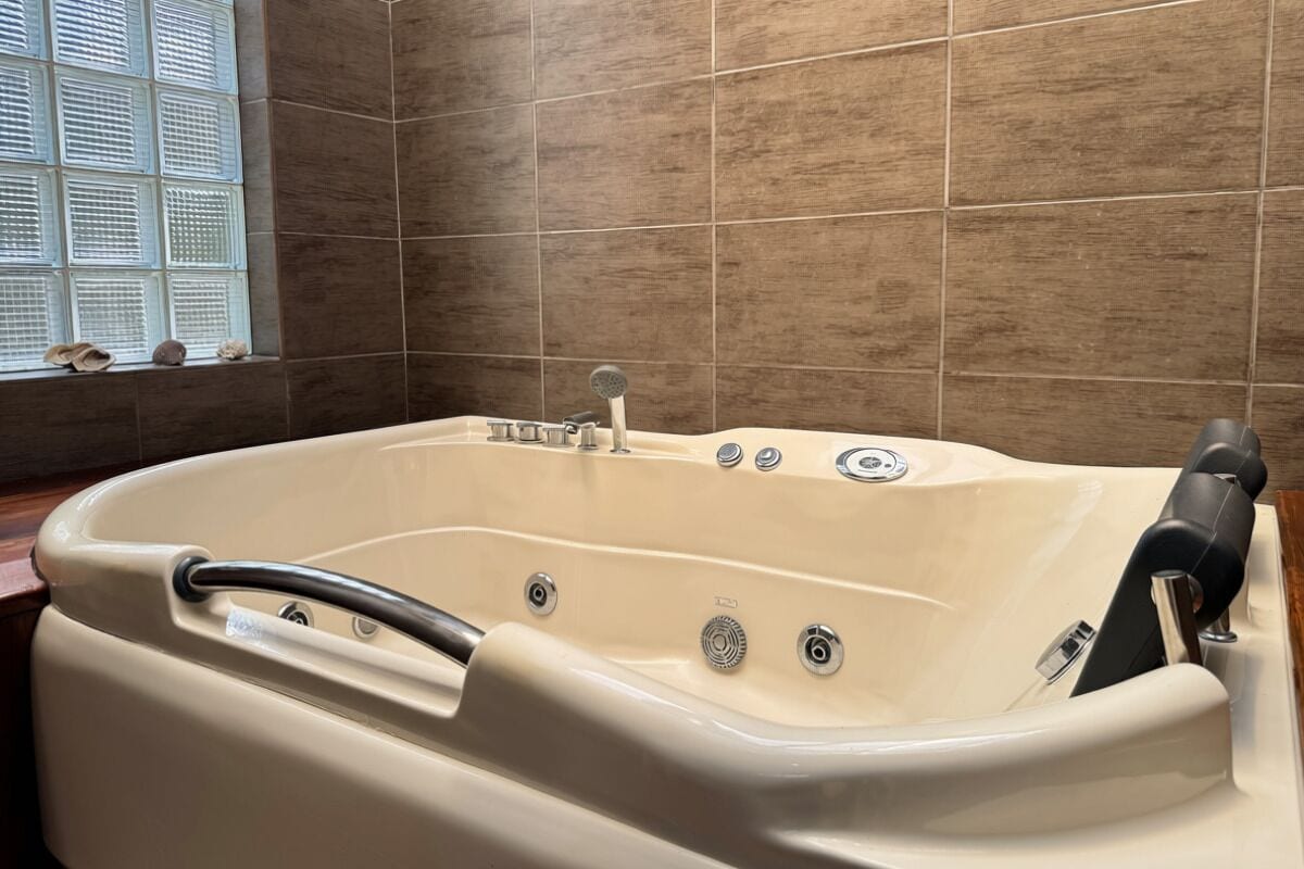 Una bañera grande y beige independiente, con asiento incorporado y cabezal de ducha de mano.