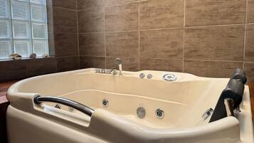 Una bañera grande y beige independiente, con asiento incorporado y cabezal de ducha de mano.