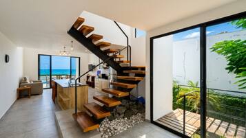 Um interior moderno com uma escada de madeira que leva a uma varanda com vista para o oceano.