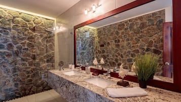 A bathroom with a stone wall, a granite countertop, a large mirror, and a potted plant.