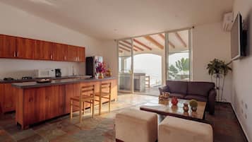 A modern kitchen with wooden cabinets, a central island with bar stools, and a dining area with a sofa and coffee table.
