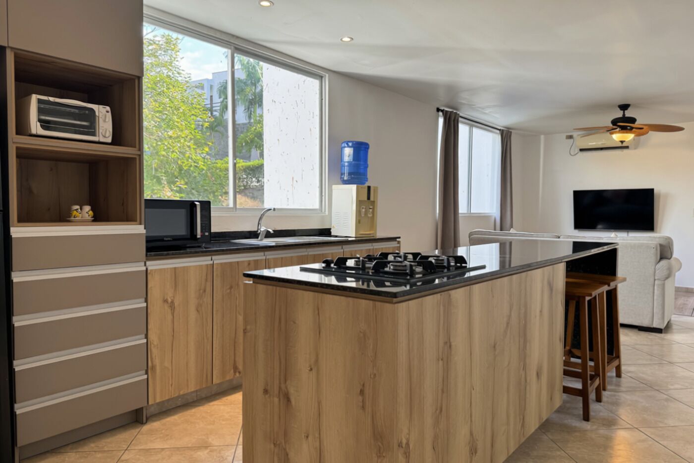 A modern kitchen with a central island, built-in appliances, and a large window providing natural light.