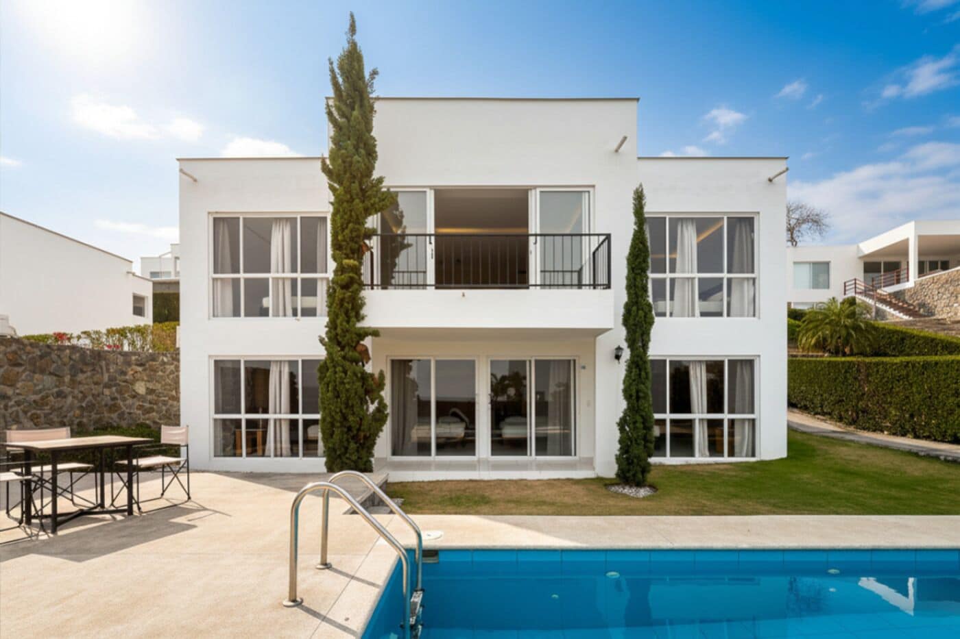 A modern two-story house with a swimming pool, large windows, and a stone wall.